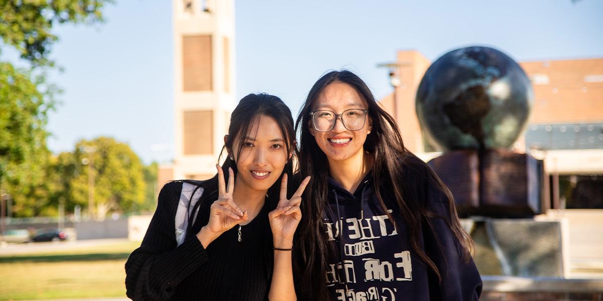 two international students posing in front of the SBU bell tower